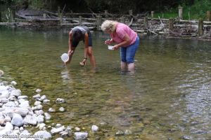 Zwei Frauen stehen in einem Gewässer und schöpfen Wasser