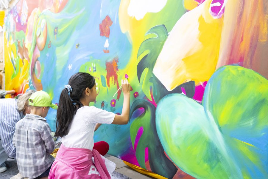 Kinder bemalen das Wandbild Mural Comunitario auf dem Bennofest 2025
