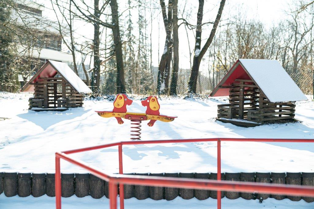 2 Spielhäuschen aus Holz und eine Federwippe im verschneiten Garten des Kinderhauses Maria Schutz