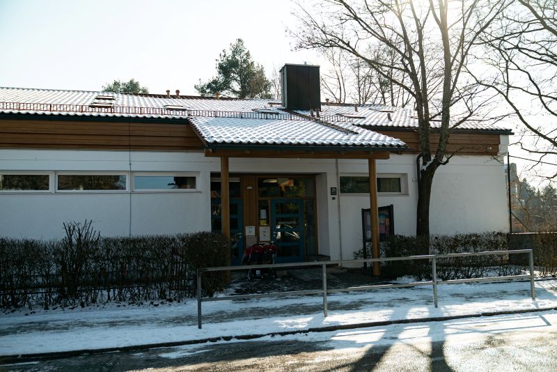 Außenansicht der Kita St. Hildegard von der Paosostraße aus. Flacher weißer Bau mit braunen Fenstern.