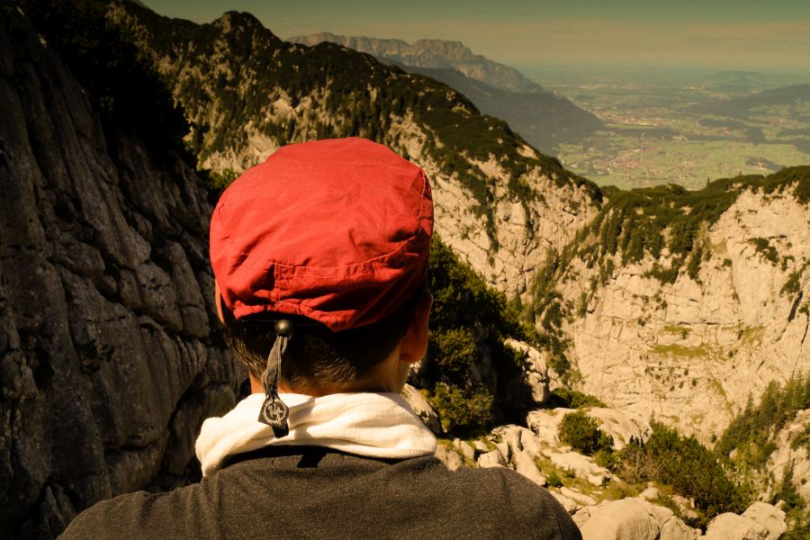 Mann steht mit dem Rücken zur Kamera hoch über einer beeindruckenden Bergkulisse