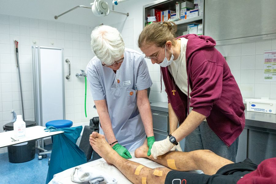 Praktikant Florian Meidinger schaut bei der Behandlung eines Obdachlosen durch eine Ärztin in Sankt Bonifaz