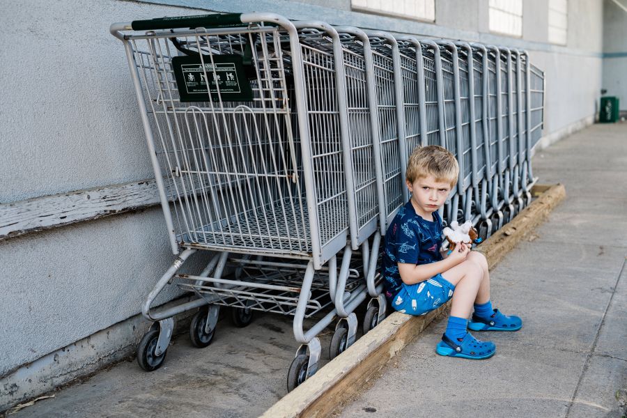 Trotziger Junge hockt vor einer Reihe von Einkaufswagen