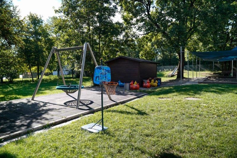 Freispielfläche im Garten der Kita St. Quirin mit Nestschaukel, Gerätehaus, Rutsche und Sandkasten