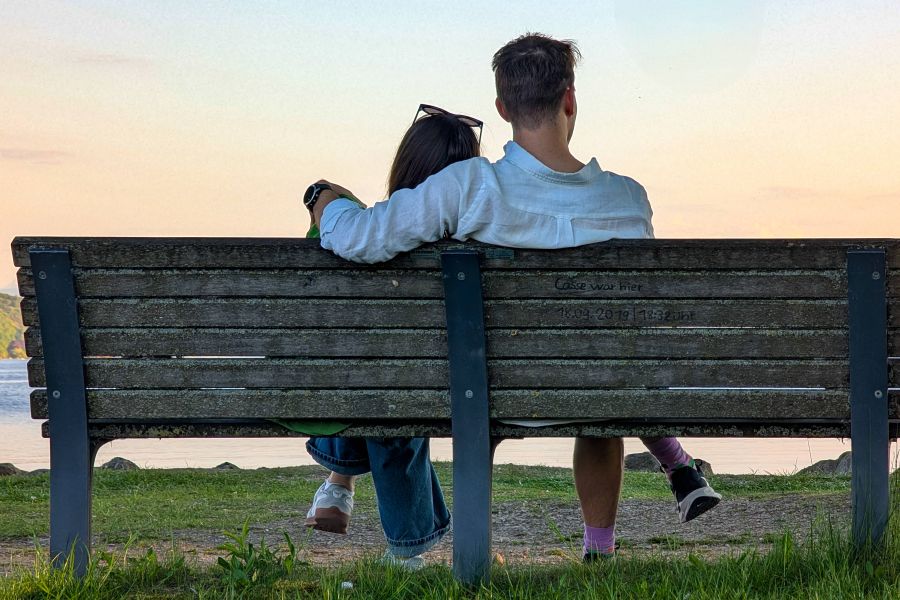 Ein Paar sitzt auf einer Bank am Starnberger See bei Sonnenuntergang.