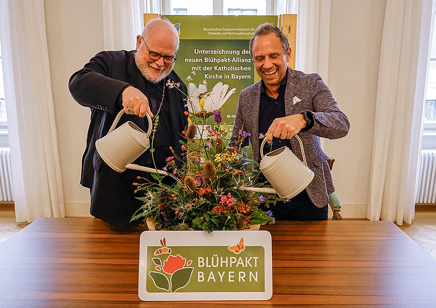 Kardinal Reinhard Marx und der bayerische Umweltminister Thorsten Glauber begießen zur Unterzeichnung des Blühpakts Bayern mit zwei Gießkannen eine Blumenvase