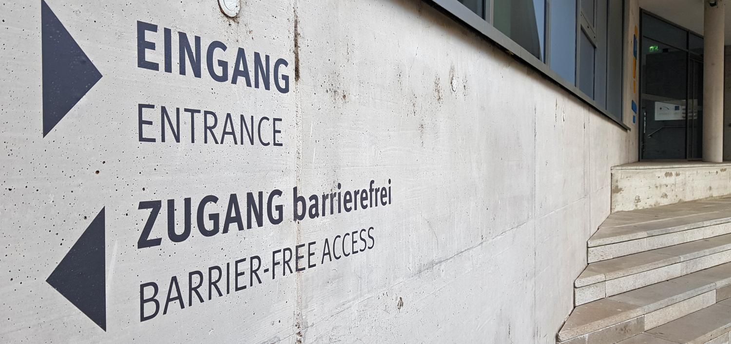 Wegweiser zu Eingang (mit Stufen) nach rechts und barrierefreiem Eingang nach links