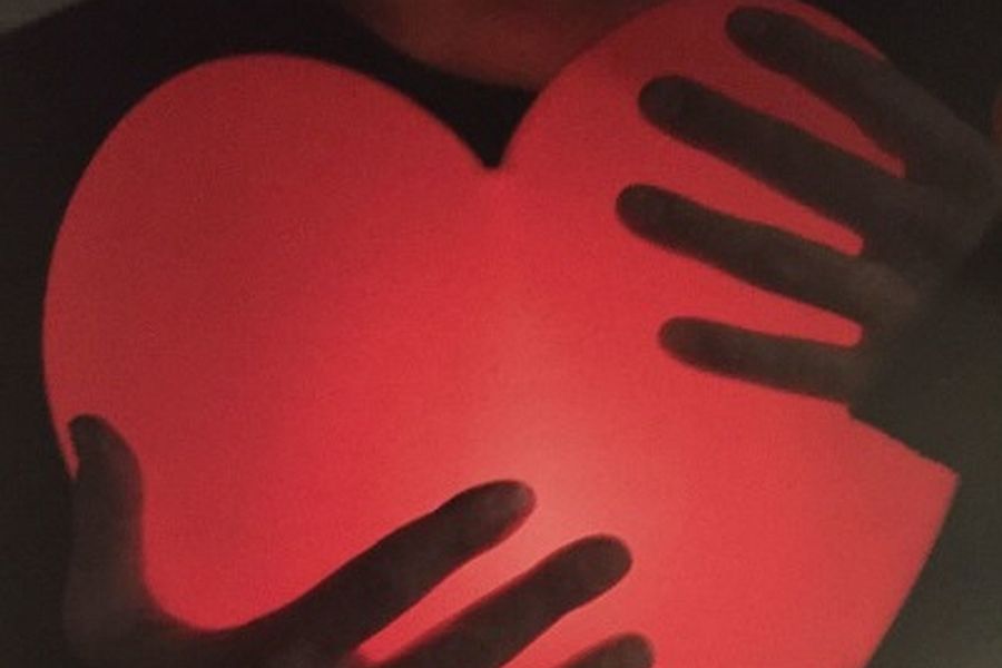 Zwei Frauenhände halten ein rot beleuchtetes Glasherz